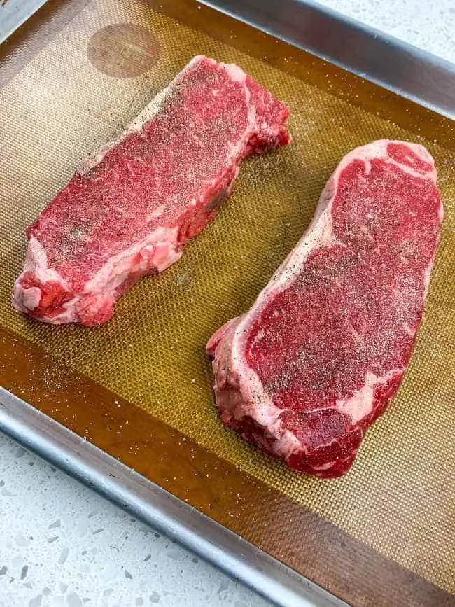 raw strip steaks on baking pan