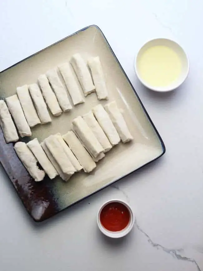Uncooked egg rolls with oil and sauce