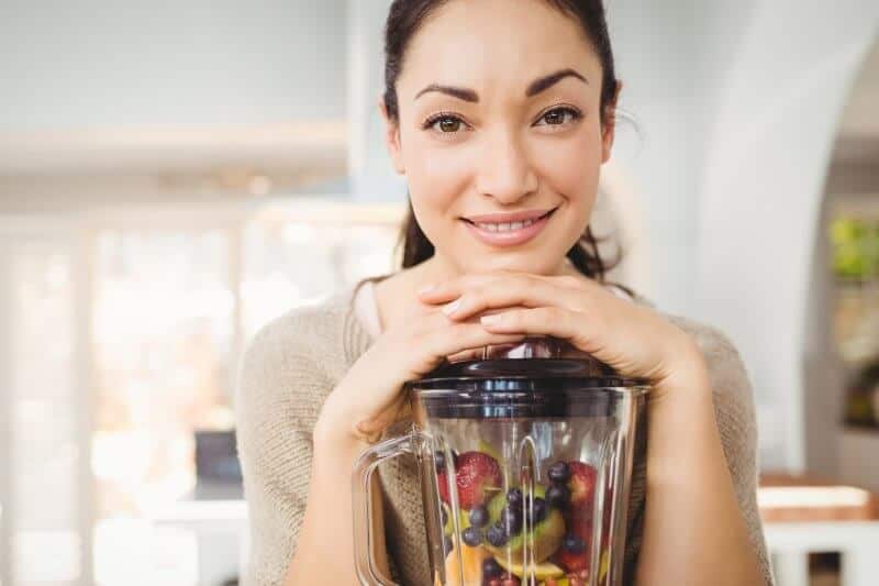 woman holding blender containing fruits