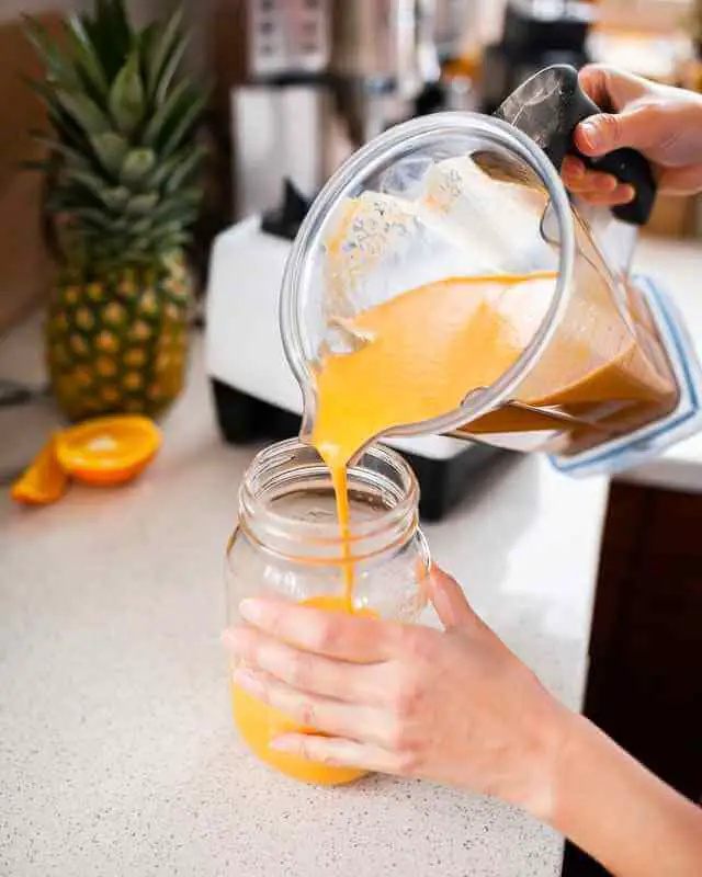 pouring orange fruit shake from blender into glass