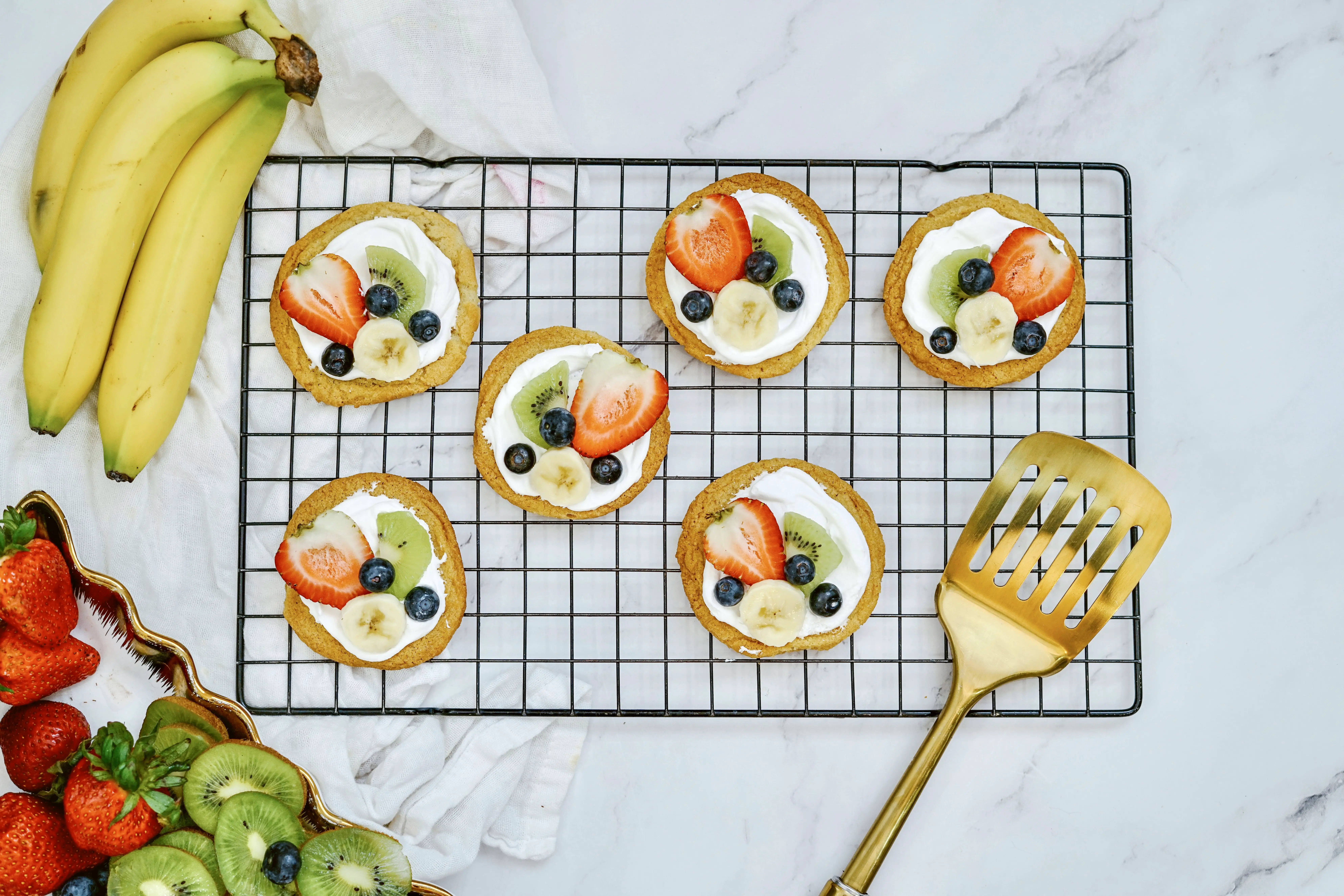 On the tiny fruit pizzas, layer the strawberry halves, kiwi slices, bananas, and blueberries.